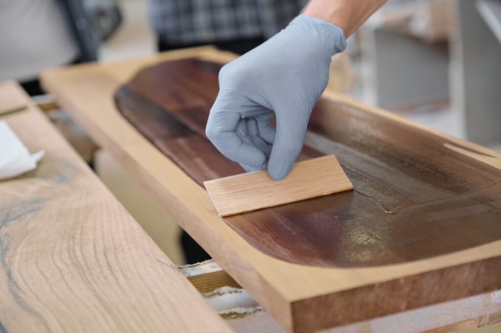 Closeup of workers hand covering wooden plank with finishing protective cover for wood